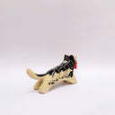 Black and cream colored ceramic sculpture of a husky dog, with a dog pack illustration on the side of its body. It holds a red tassel in its mouth with a small bronze bell.
