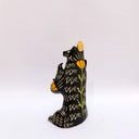 Ceramic figurine of a black bear, with its arms cradling 2 small animals - a miniature deer and a miniature buffalo. The bear has 2 ravens on its shoulders and a gold coin atop its head.