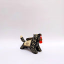Ceramic sculpture of a black wolf with sgraffito cream colored fur lines, holding a red tassel in its mouth. On its back rests a cream colored blanket with a doll charm laying atop it.