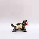 Ceramic sculpture of a black wolf with sgraffito cream colored fur lines, holding a red tassel in its mouth. On its back rests a cream colored blanket with a doll charm laying atop it.