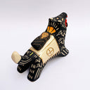 Ceramic sculpture of a black wolf with sgraffito cream colored fur lines, holding a red tassel in its mouth. On its back rests a cream colored blanket with a doll charm laying atop it.