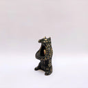 Black and cream colored ceramic sculpture of a bear, sitting on its hind legs with its arms cradled together. It has a recession in its chest where an oval shaped pennant with a red heart hangs. 