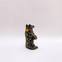Black and cream colored ceramic sculpture of a bear, sitting on its hind legs with its arms cradled together. It has a recession in its chest where an oval shaped pennant with a red heart hangs. 