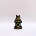 Black and cream colored ceramic sculpture of a bear, sitting on its hind legs with its arms cradled together. It has a recession in its chest where an oval shaped pennant with a red heart hangs. 