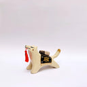 Ceramic sculpture of a cream colored wolf, with a red tassel hanging from its mouth and a black and gold blanket on its back. Atop the blanket is a wrapped doll charm.
