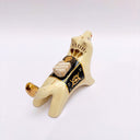 Ceramic sculpture of a cream colored wolf, with a red tassel hanging from its mouth and a black and gold blanket on its back. Atop the blanket is a wrapped doll charm.