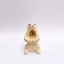 Cream colored ceramic sculpture of a bear, sitting on its hind legs with its arms cradled together. It has a recession in its chest where a gold star hangs. 