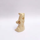 Cream colored ceramic sculpture of a bear, sitting on its hind legs with its arms cradled together. It has a recession in its chest where a gold star hangs. 