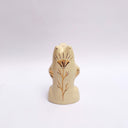 Cream colored ceramic sculpture of a bear, sitting on its hind legs with its arms cradled together. It has a recession in its chest where a gold star hangs. 