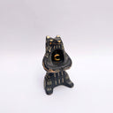 Black and cream colored ceramic sculpture of a bear, sitting on its hind legs with its arms cradled together. It has a recession in its chest where a gold crescent moon hangs. 