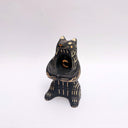 Black and cream colored ceramic sculpture of a bear, sitting on its hind legs with its arms cradled together. It has a recession in its chest where a gold crescent moon hangs. 