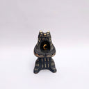 Black and cream colored ceramic sculpture of a bear, sitting on its hind legs with its arms cradled together. It has a recession in its chest where a gold crescent moon hangs. 