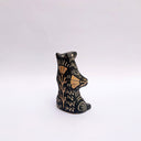 Black and cream colored ceramic sculpture of a bear, sitting on its hind legs with its arms cradled together. It has a recession in its chest where a gold crescent moon hangs. 