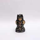 Black and cream colored ceramic sculpture of a bear, sitting on its hind legs with its arms cradled together. It has a recession in its chest where a gold crescent moon hangs. 