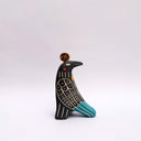 Ceramic sculpture of a black bird, with sgraffito wing patterning to reveal a cream colored clay, with blue and orange color detailing. It has a poppy flower on its back and a coin atop its head.