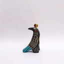 Ceramic sculpture of a black bird, with sgraffito wing patterning to reveal a cream colored clay, with blue and orange color detailing. It has a poppy flower on its back and a coin atop its head.