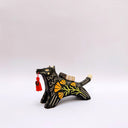 A black ceramic figurine of a wolf carrying a red tassel charm in its mouth, decorated with yellow and orange floral patterns and a small wrapped doll charm on its back, set against a plain light gray background.