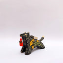 A black ceramic figurine of a wolf carrying a red tassel charm in its mouth, decorated with yellow and orange floral patterns and a small wrapped doll charm on its back, set against a plain light gray background.