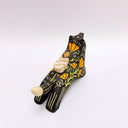 A black ceramic figurine of a wolf carrying a red tassel charm in its mouth, decorated with yellow and orange floral patterns and a small wrapped doll charm on its back, set against a plain light gray background.