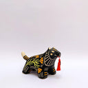 Ceramic sculpture of a black wolf/tiger like animal, on all fours with cream colored sgraffito detailing and poppy flower patterings on its body. It has a red tassel in its mouth.