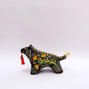 Ceramic sculpture of a black wolf/tiger like animal, on all fours with cream colored sgraffito detailing and poppy flower patterings on its body. It has a red tassel in its mouth.
