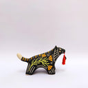 Ceramic sculpture of a black wolf/tiger like animal, on all fours with cream colored sgraffito detailing and poppy flower patterings on its body. It has a red tassel in its mouth.