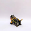 Ceramic sculpture of a black wolf/tiger like animal, on all fours with cream colored sgraffito detailing and poppy flower patterings on its body. It has a red tassel in its mouth.