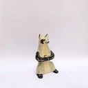Ceramic sculpture of a cream and gray fox with black accent colorings, sitting up on its hind legs with its arms together in a cradling pose. Resting in its arms is a small wrapped doll.