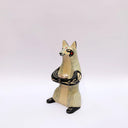 Ceramic sculpture of a cream and gray fox with black accent colorings, sitting up on its hind legs with its arms together in a cradling pose. Resting in its arms is a small wrapped doll.