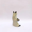 Ceramic sculpture of a cream and gray fox with black accent colorings, sitting up on its hind legs with its arms together in a cradling pose. Resting in its arms is a small wrapped doll.