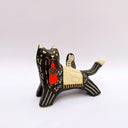 A ceramic black wolf figurine with cream-colored stripes, a red tassel ornament that hangs from its mouth, and a small owl perched on its back atop of an astronomy themed blanket, photographed against a plain light background.