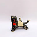 A ceramic black wolf figurine with cream-colored stripes, a red tassel ornament that hangs from its mouth, and a small owl perched on its back atop of an astronomy themed blanket, photographed against a plain light background.