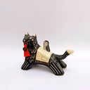 A ceramic black wolf figurine with cream-colored stripes, a red tassel ornament that hangs from its mouth, and a small owl perched on its back atop of an astronomy themed blanket, photographed against a plain light background.