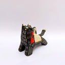 A ceramic black wolf figurine with cream-colored stripes, a red tassel ornament that hangs from its mouth, and a small owl perched on its back atop of an astronomy themed blanket, photographed against a plain light background.