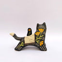 A ceramic black wolf figurine with cream-colored stripes, a red tassel ornament that hangs from its mouth, and a small owl perched on its back atop of an astronomy themed blanket, photographed against a plain light background.
