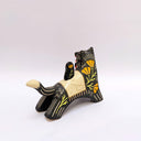 A ceramic black wolf figurine with cream-colored stripes, a red tassel ornament that hangs from its mouth, and a small owl perched on its back atop of an astronomy themed blanket, photographed against a plain light background.