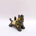 A ceramic black wolf figurine with cream-colored stripes, a red tassel ornament that hangs from its mouth, and a small owl perched on its back atop of an astronomy themed blanket, photographed against a plain light background.