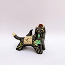 Ceramic sculpture of a black wolf with sgraffito line art and fur texture, with floral patterning. It has a cream colored blanket on its back, with a small bird sitting atop of it.