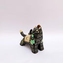 Ceramic sculpture of a black wolf with sgraffito line art and fur texture, with floral patterning. It has a cream colored blanket on its back, with a small bird sitting atop of it.