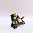 Ceramic sculpture of a black wolf with sgraffito line art and fur texture, with floral patterning. It has a cream colored blanket on its back, with a small bird sitting atop of it.