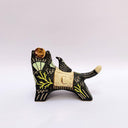 Ceramic sculpture of a black wolf with sgraffito line art and fur texture, with floral patterning. It has a cream colored blanket on its back, with a small bird sitting atop of it.