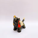 Ceramic sculpture of a black wolf with sgraffito line art for its fur and patterning. It hold a red tassel and charm in its mouth and has a blanket on its back. Sitting on the blanket is a small bird.