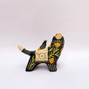 Ceramic sculpture of a black wolf with sgraffito line art for its fur and patterning. It hold a red tassel and charm in its mouth and has a blanket on its back. Sitting on the blanket is a small bird.