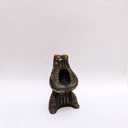 Black ceramic sculpture of a wolf/bear animal, sitting up on its hind legs, with its arms cradled together. There is a recession in its chest. It has subtle poppy flower designs on it.