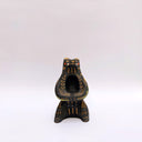Black ceramic sculpture of a wolf/bear animal, sitting up on its hind legs, with its arms cradled together. There is a recession in its chest. It has subtle poppy flower designs on it.