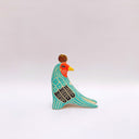 A stylized bird figurine in turquoise, cream, black, red, yellow, and brown, with a gold coin atop its head, photographed on a plain light gray background.