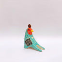 A stylized bird figurine in turquoise, cream, black, red, yellow, and brown, with a gold coin atop its head, photographed on a plain light gray background.