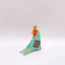 A stylized bird figurine in turquoise, cream, black, red, yellow, and brown, with a gold coin atop its head, photographed on a plain light gray background.