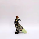 Ceramic sculpture of a black billed magpie, with stylized feather patterning in cream and mint green. On its back is a poppy flower and atop its head is a gold coin.