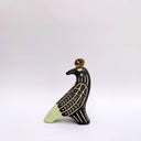 Ceramic sculpture of a black billed magpie, with stylized feather patterning in cream and mint green. On its back is a poppy flower and atop its head is a gold coin.